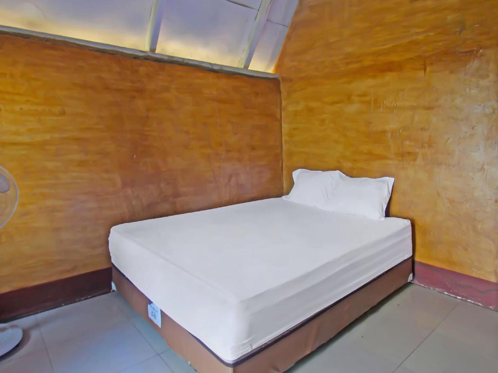 Cama blanca en habitación con pared de madera en OYO 92419 Rejeng Homestay Near Kerta Gangga Waterfall en Luk