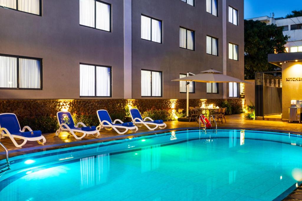 a swimming pool with chairs and an umbrella and a building at Saggys Suites Hotel & Spa in Nairobi