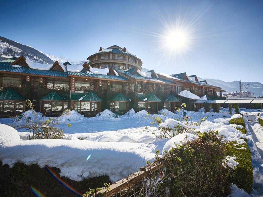 a building covered in snow with the sun behind it at Club Mahindra White Meadows Manali in Nagar