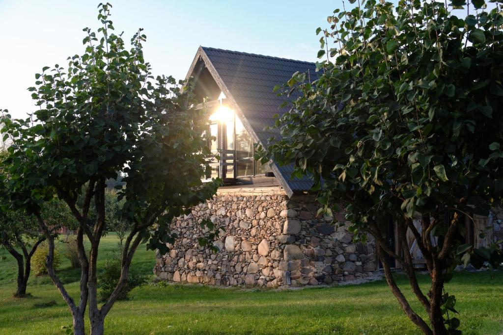 a stone house with a stone wall and trees at Ugunu Dambji in Talsi