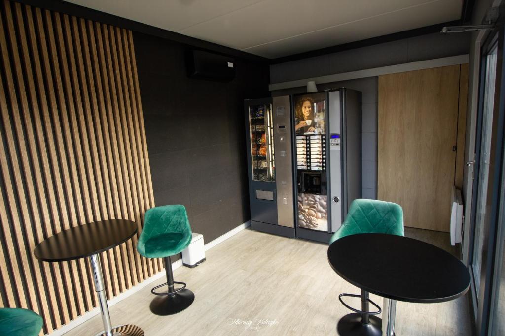 Small lounge with vending machines, green velvet bar chairs and black round tables against slatted wall.