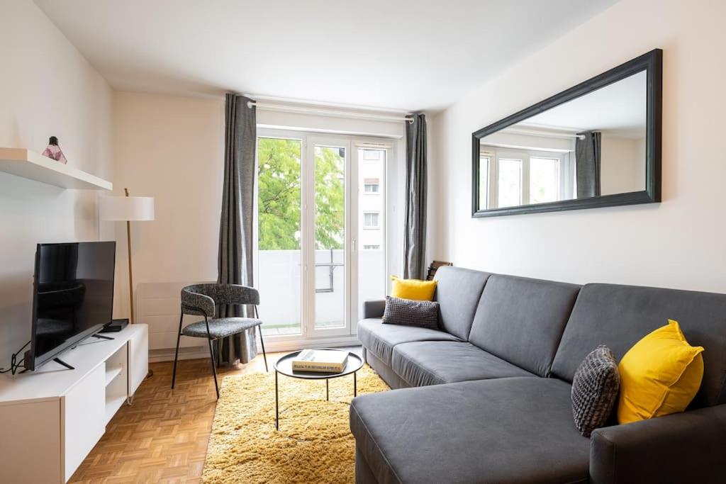 - un salon avec un canapé gris et un miroir dans l'établissement L’Ébène-Paris, Stade de France, Parking & Balcon, à Saint-Denis