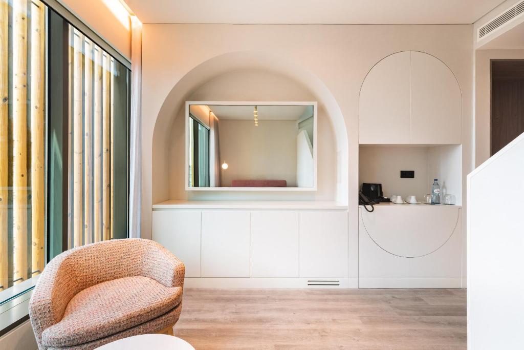 A compact sitting and refreshment area with an armchair, mirror, minibar niche, and window.