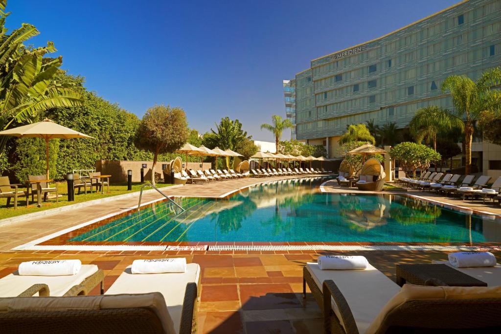 a swimming pool with lounge chairs and a hotel at Le Meridien Cairo Airport in Cairo