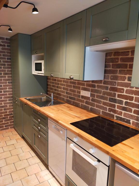 une cuisine avec des placards verts et un mur en briques dans l'établissement Charme et confort à proximité du vieux bassin, à Honfleur