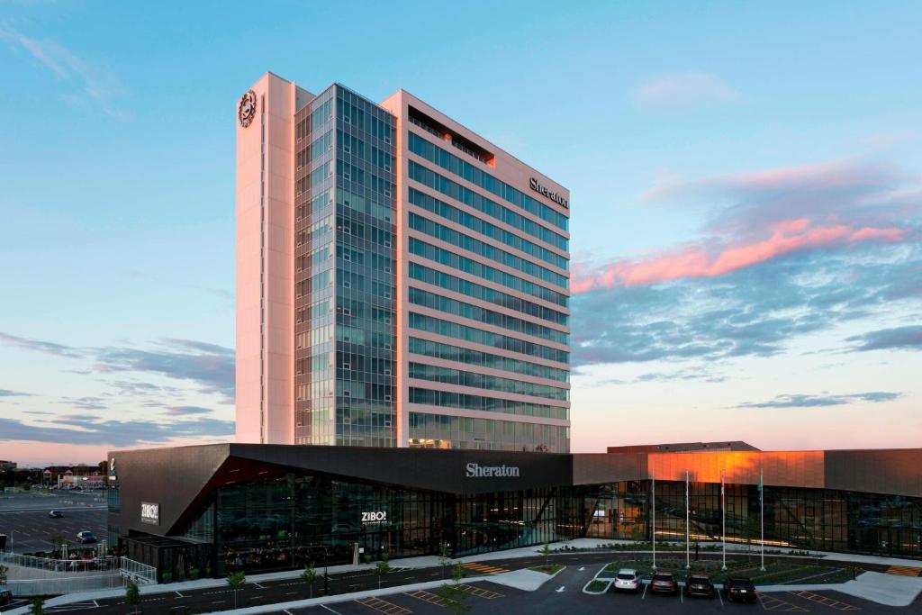 Sheraton Saint-Hyacinthe Hotel في سان هياسنت: مبنى طويل أمام موقف للسيارات