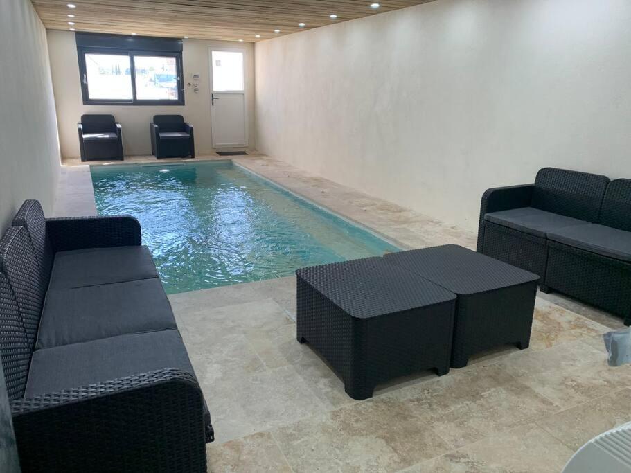 a swimming pool with chairs and a couch and a table at Villa piscine/spa privé intérieur 33° ZOO DE LA FLECHE 24h DU MANS in La Flèche