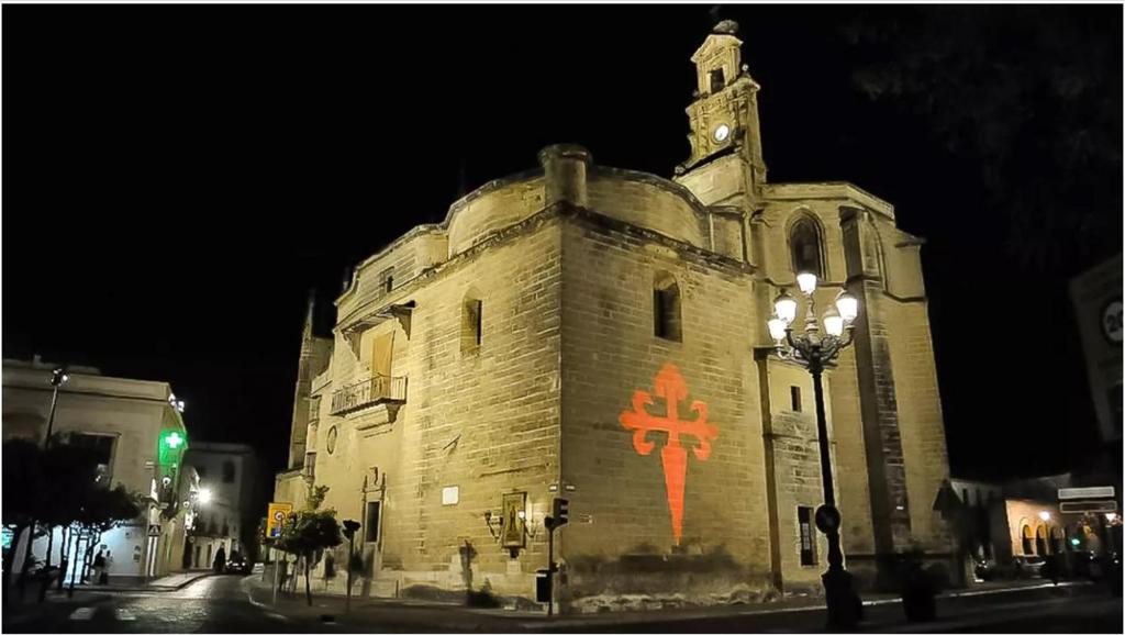 um velho edifício de pedra com uma cruz vermelha pintada nele em APARTAMENTOS IGLESIA DE SANTIAGo II em Jerez de la Frontera