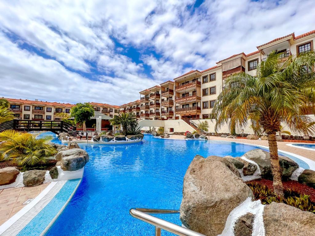 a pool at a resort with palm trees and buildings at Seaside apartment with a sea view in Costa Del Silencio