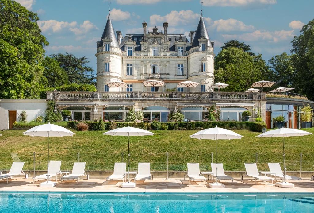 einen Pool vor einem Schloss mit Stühlen und Sonnenschirmen in der Unterkunft Domaine de la Tortinière in Montbazon