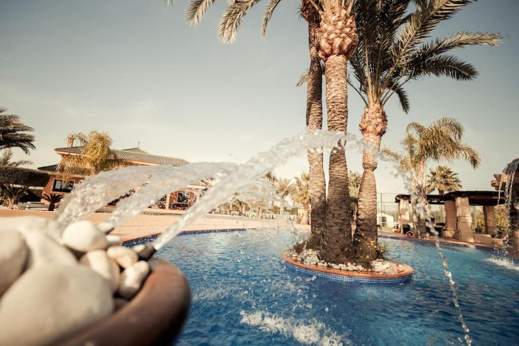 a water fountain in a swimming pool with palm trees at Villa san jaime in Daimés