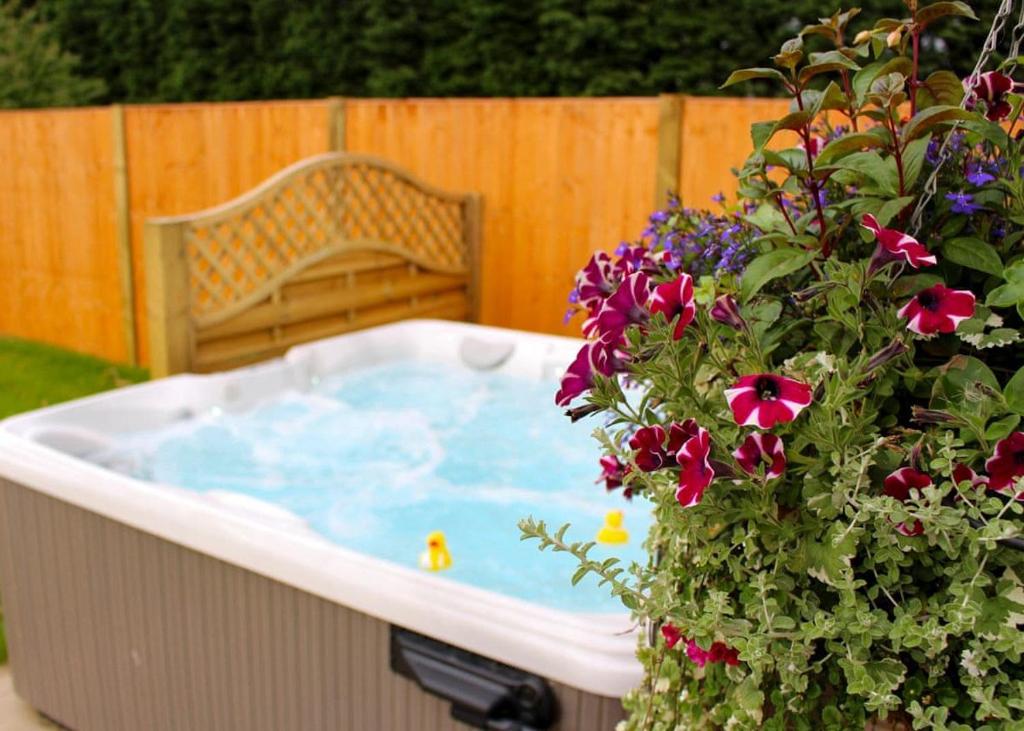 a jacuzzi tub in a yard with a bench and flowers at Beech Tree Lakes Lodges in Hatfield