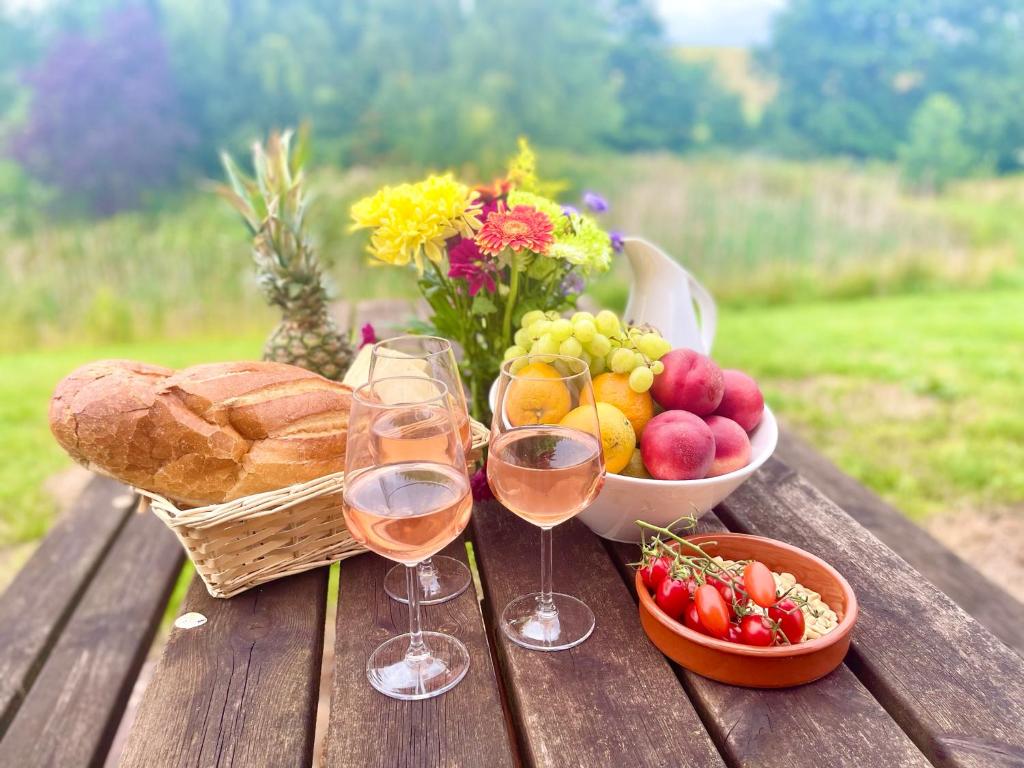 a picnic table with two glasses of wine and a basket of fruit at Cedar Barn in Llangwm-isaf