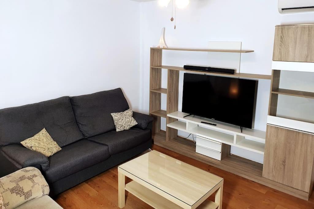 a living room with a black couch and a flat screen tv at 4F, Aire Acondic, 80m2, 2 dormitorios, 4 huéspedes, WIFI GRATIS in La Línea de la Concepción