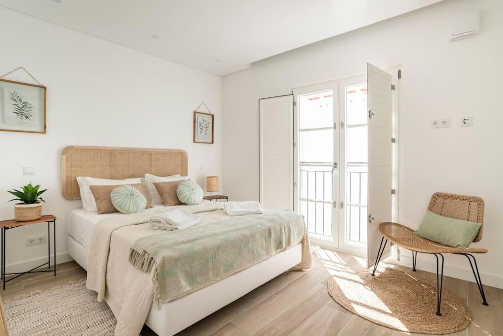 a white bedroom with a bed and a chair at Casa Nova do Levante, perto do Mar, com estacionamento privativo in Olhão