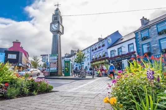 una torre dell'orologio nel bel mezzo di una città con dei fiori di Dun Maeve Guesthouse a Westport