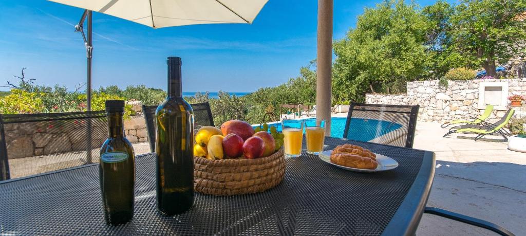 a table with a basket of fruit and two bottles of wine at Mljet, old stone apartment with pool in nature in Babino Polje