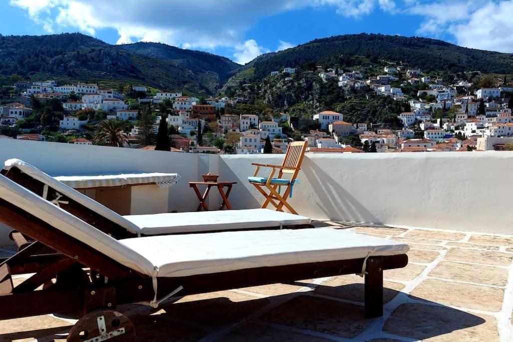 a balcony with a bench and a chair and a city at Christina's Stone House Apartment in Hydra