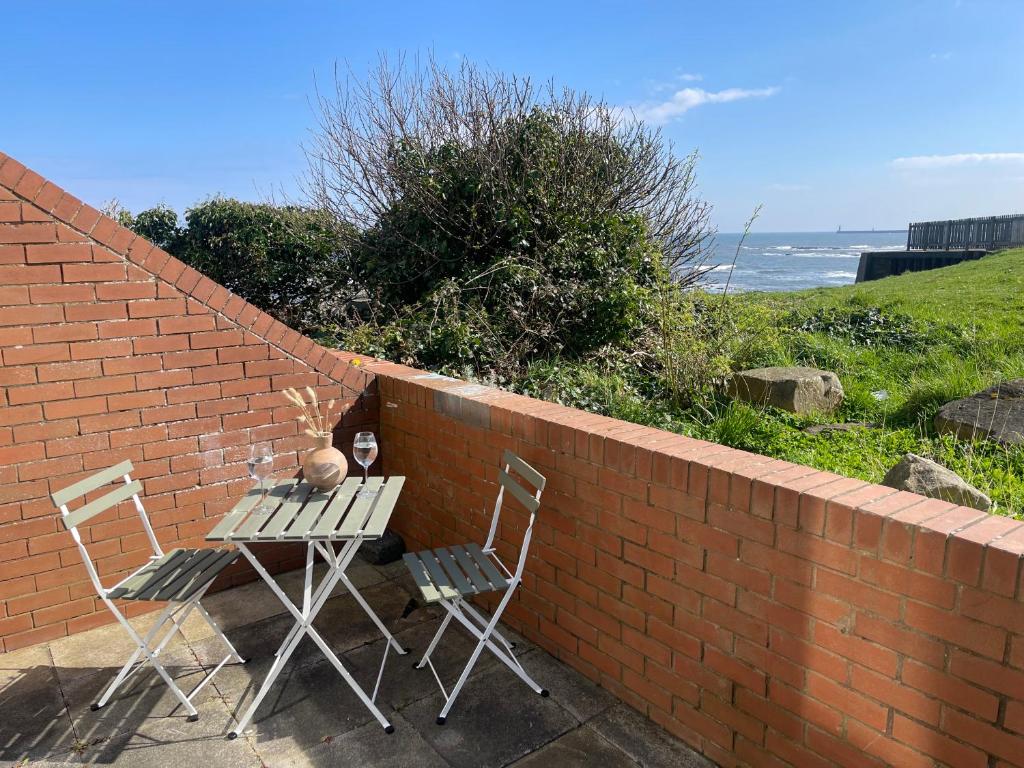 a table and chairs sitting next to a brick wall at Cliff Haven, Sea View Holiday Home. in Cullercoats