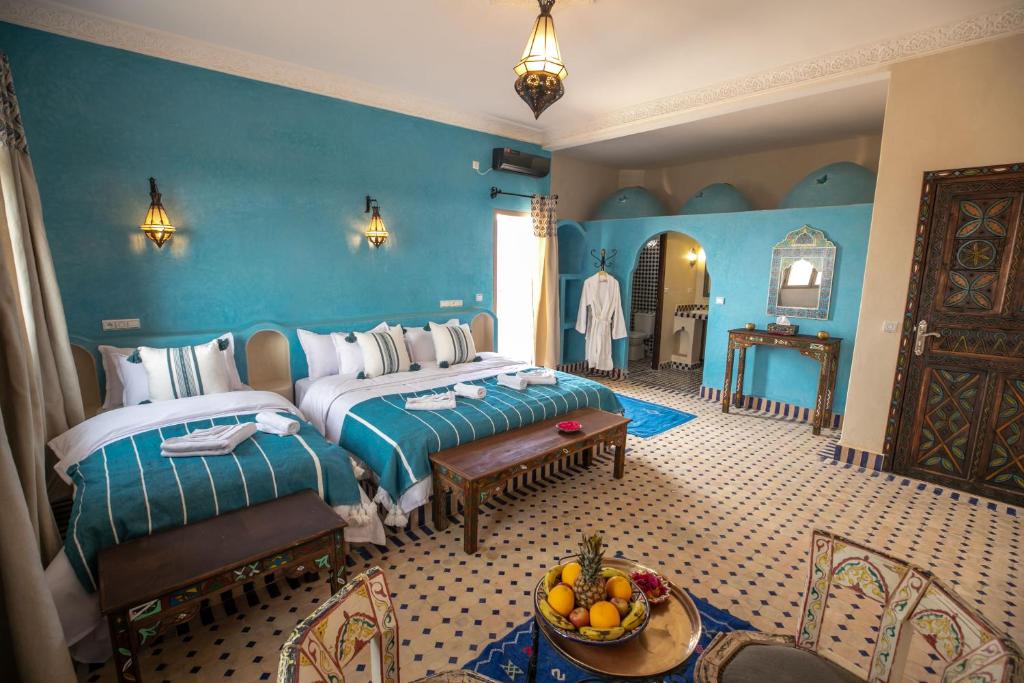 Un dormitorio con 2 camas y una mesa con un bol de fruta en Riad Jouba, en Merzouga