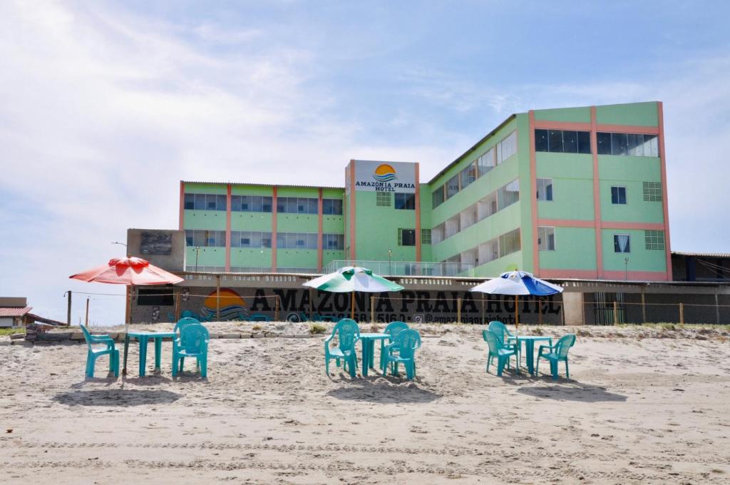 a group of chairs and tables on a beach with a building at Amazônia Praia Hotel in Tibau