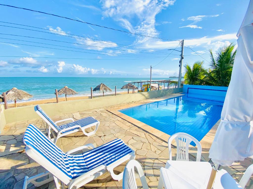 una piscina con sedie e l'oceano sullo sfondo di Casablanca Beira Mar, 5 Suítes, Praia Tabuba AL a Barra de Santo Antônio