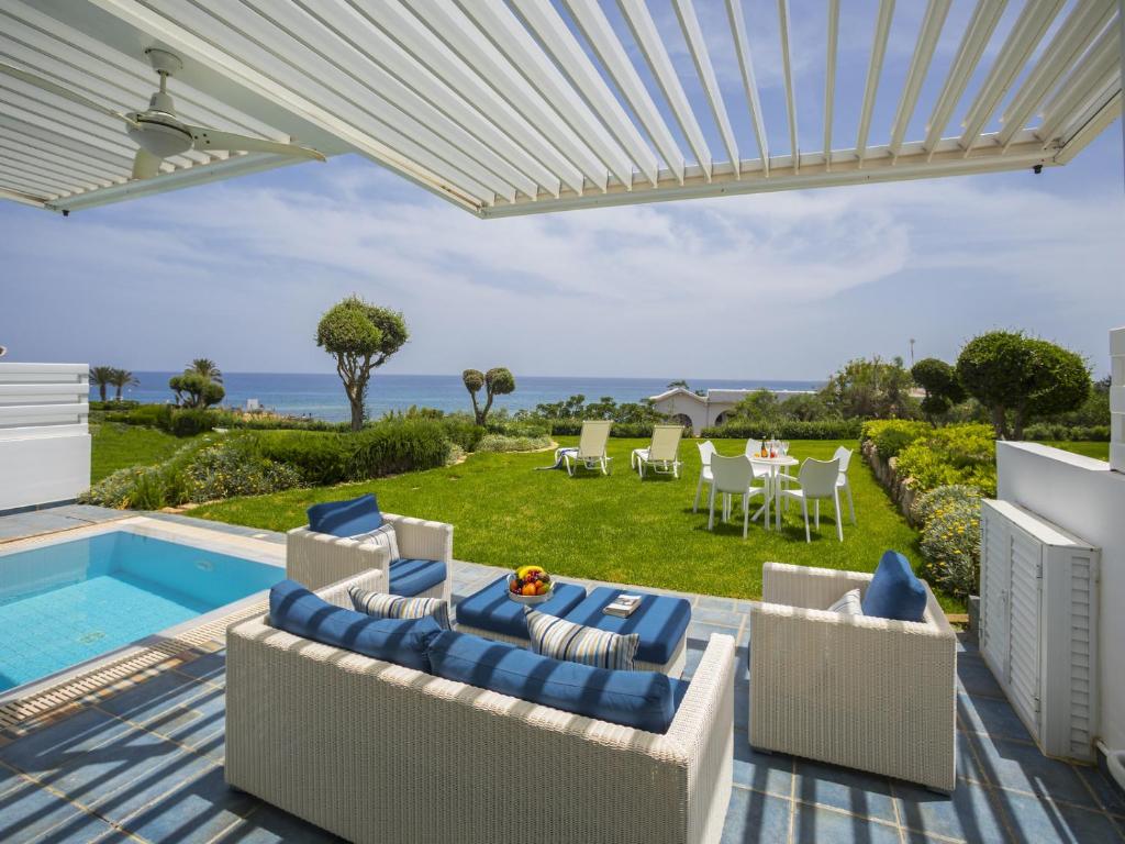 a patio with chairs and a swimming pool with a view of the ocean at Protaras Seafront Villa Sirina Pearl in Protaras