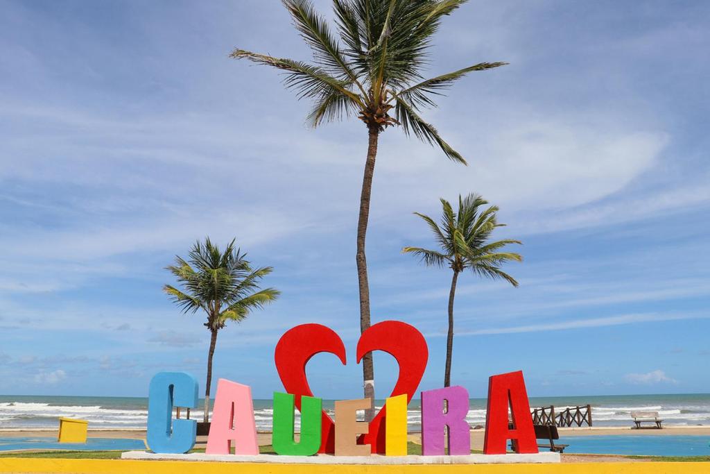 a colorful sign on a beach with palm trees at Casa de andar a 200m da areia Praia da Caueira SE in Praia Da Caueira