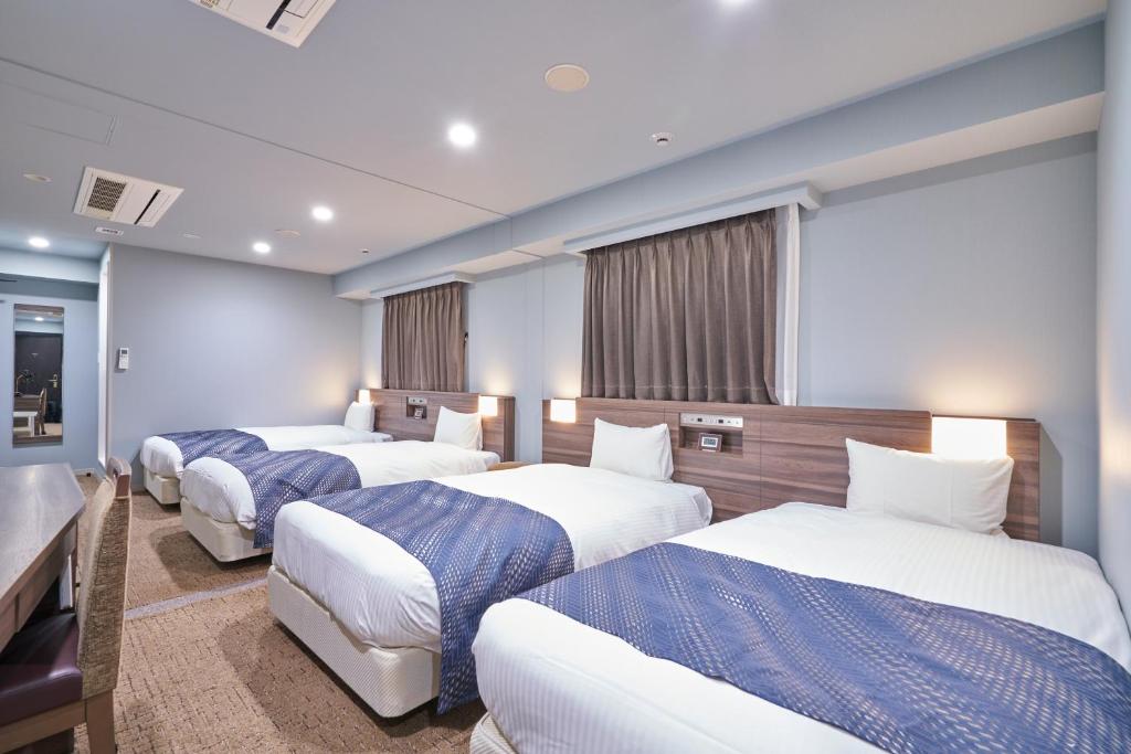 a hotel room with three beds and a television at HOTEL VINE OSAKA KITAHAMA in Osaka