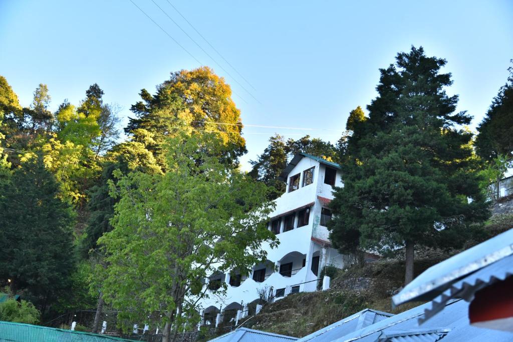 a white building on top of a hill with trees at Kumaon Roop Resort Near Neem Karoli Temple in Nainital