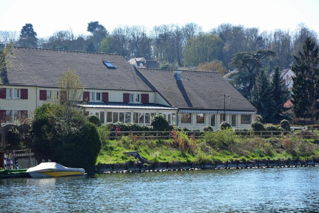 une maison sur la rive d'une rivière avec un bateau dans l'établissement Logis Hôtel des Lacs Paris Sud, à Viry-Châtillon