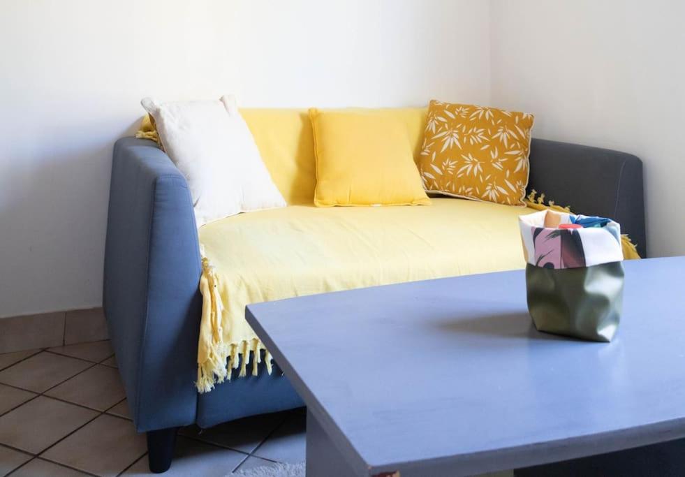 Sofá azul con almohadas amarillas y mesa en PETIT NID COSY - Proche des ecoles et entreprises, en Orsay