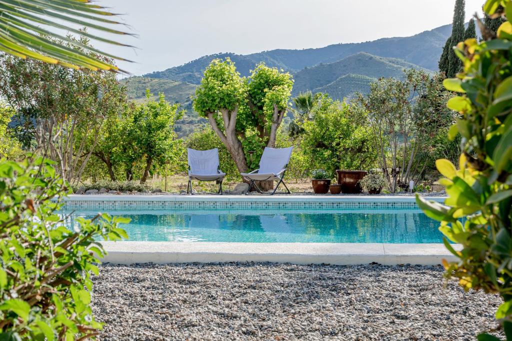 een zwembad met twee stoelen en bomen en bergen bij Finca El Limonar in Alora