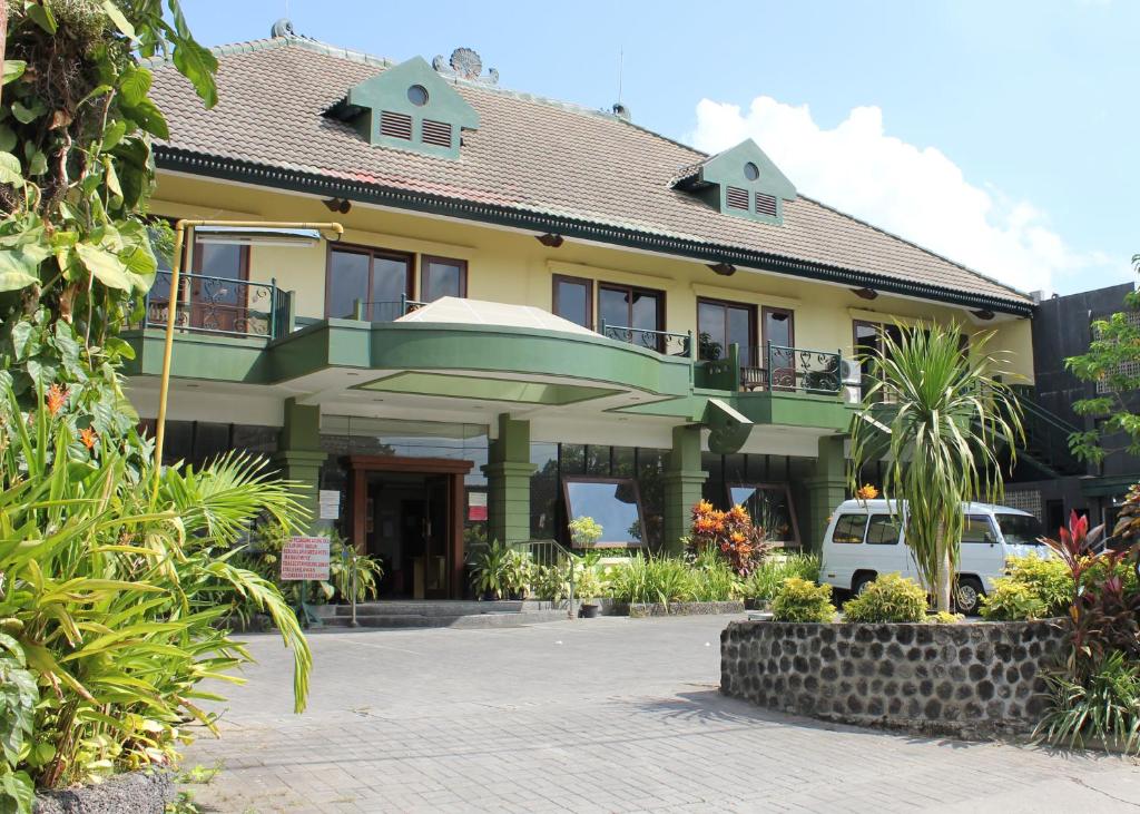 un bâtiment jaune et vert avec une voiture garée devant dans l'établissement Hotel Winotosastro Garden, à Yogyakarta