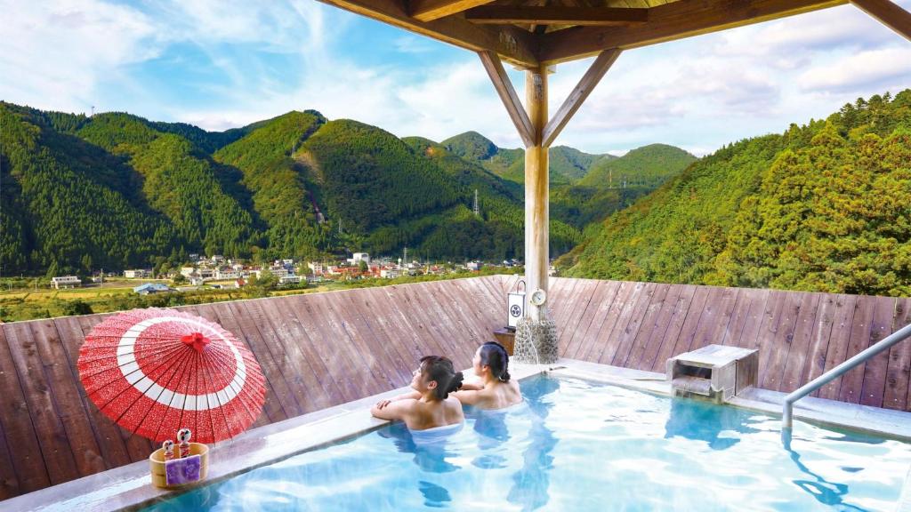 dos personas en una piscina con montañas en el fondo en Ooedo Onsen Monogatari Masuya, en Osaki