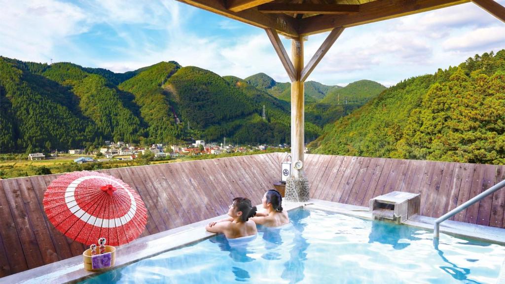 two people in a swimming pool with mountains in the background at Ooedo Onsen Monogatari Masuya in Osaki