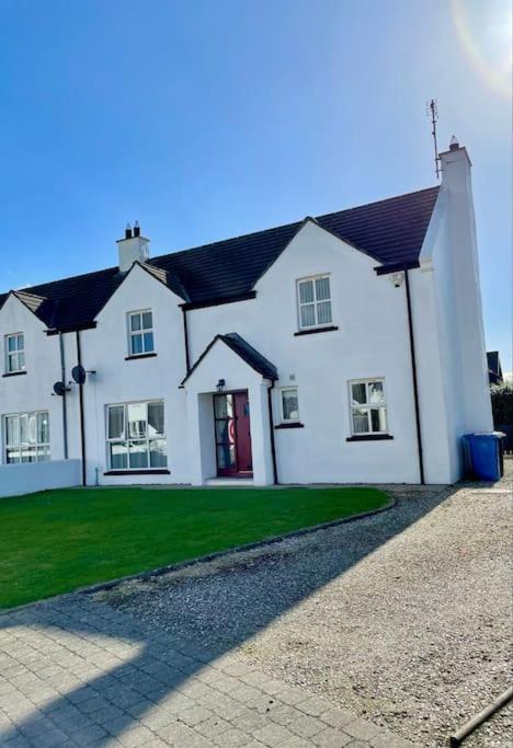 a white house with a red door and grass at Pear Tree Cottage, Portstewart in Portstewart