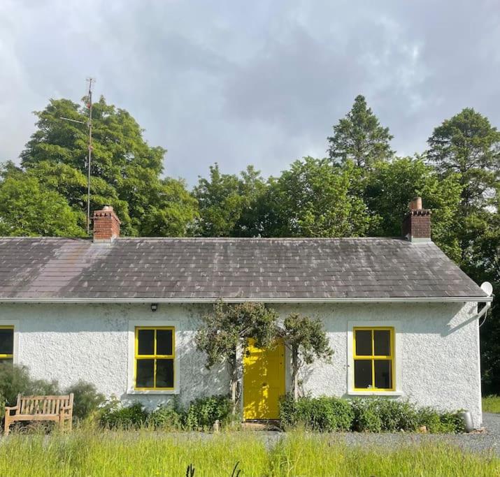 ein weißes Haus mit einer gelben Tür und einer Bank in der Unterkunft Newly renovated Cottage with private trout fishing set in beautiful wildlife estate in Monaghan
