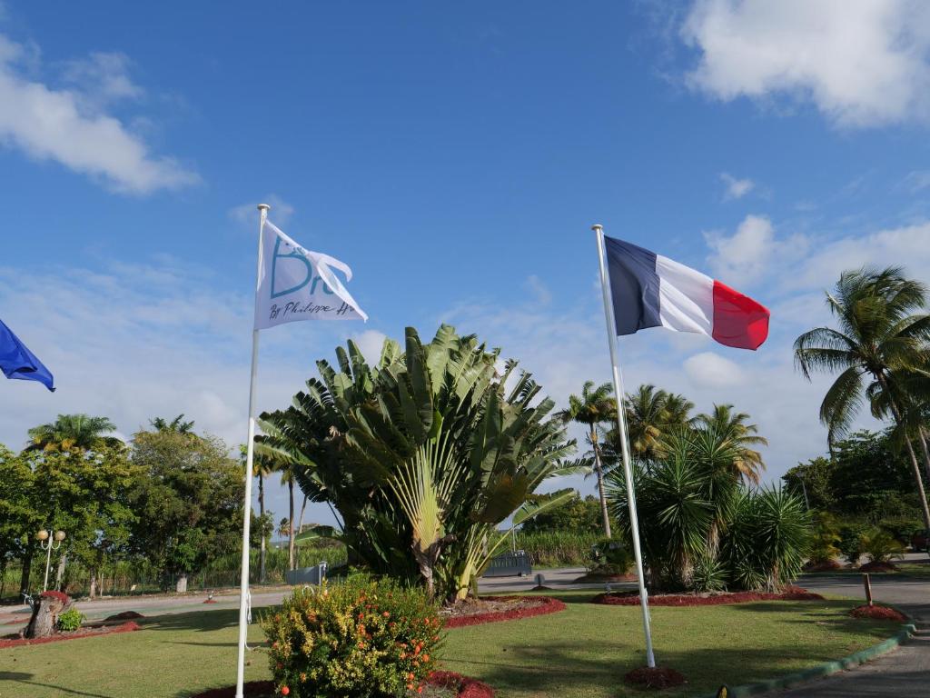 two flags on poles in a park with palm trees at Village Kawann - Toumalacai 246 in Grand-Bourg