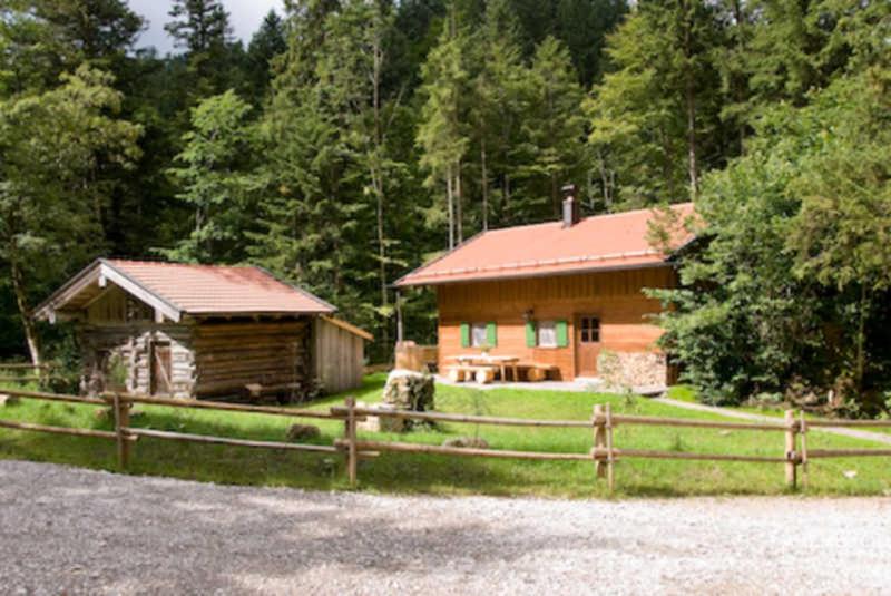 une cabane en rondins avec une clôture et une maison dans l'établissement Almhaus Webermohof, à Rottach-Egern