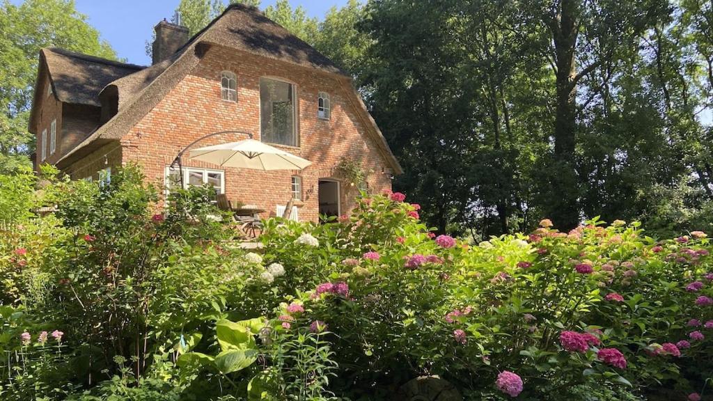 a brick house with an umbrella in a garden at Reetdachhaus Warft Simmerdeis - Maisonettewohnung in Oldenswort
