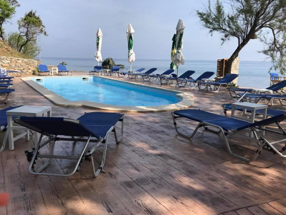 a swimming pool with chaise lounge chairs and the ocean at Hotel Kokkino Nero in Kókkinon Nerón