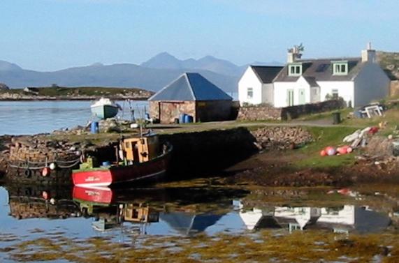 a boat sitting in the water next to a house at Pier Cottage, Applecross in Applecross