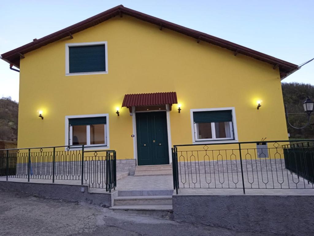 a yellow house with a green door and a fence at Milky's House in Isola del Cantone