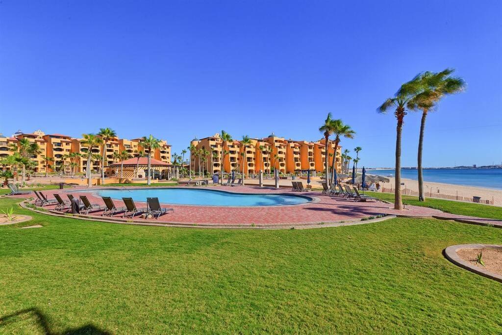 a resort pool with chairs and palm trees and the beach at Sandy Beach Princesa A103 Ocean Front Resort in Puerto Peñasco