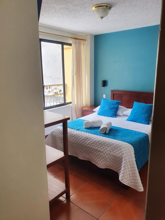 1 Schlafzimmer mit 2 Betten mit blauen Wänden und einem Fenster in der Unterkunft Hostal CañaLimeña in Baños