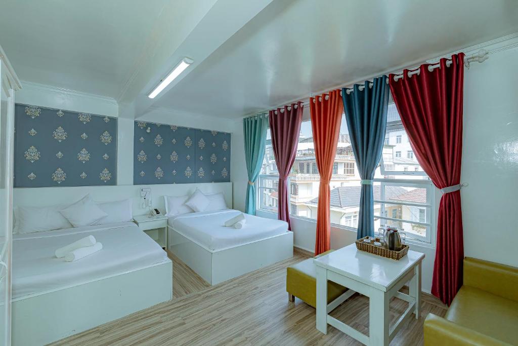 Cette chambre comprend 2 lits, une table et des fenêtres. dans l'établissement Ken's Backpackers Hotel, à Đà Lạt