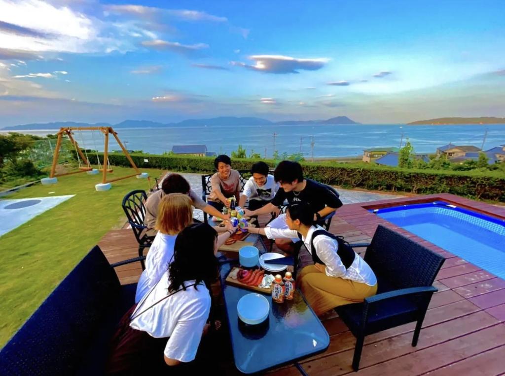Seaside Villa SASAO - Vacation STAY 33407v في Sanuki: مجموعة من الناس يجلسون حول طاولة بجانب مسبح