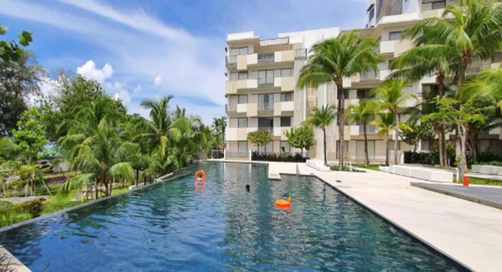 a swimming pool in front of a building with palm trees at By The Sea Batu Ferringhi in Batu Ferringhi