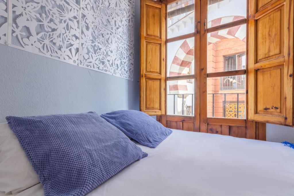 a bed with blue pillows in a room with a window at Apartamento Ilusión Andaluza in Córdoba